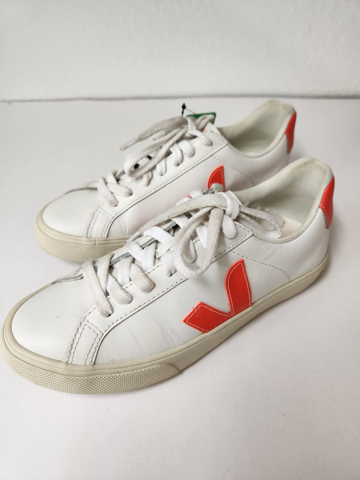 A pair of white leather low-top sneakers with a signature red V logo on the side, white laces, and off-white soles, shown on a plain light background.