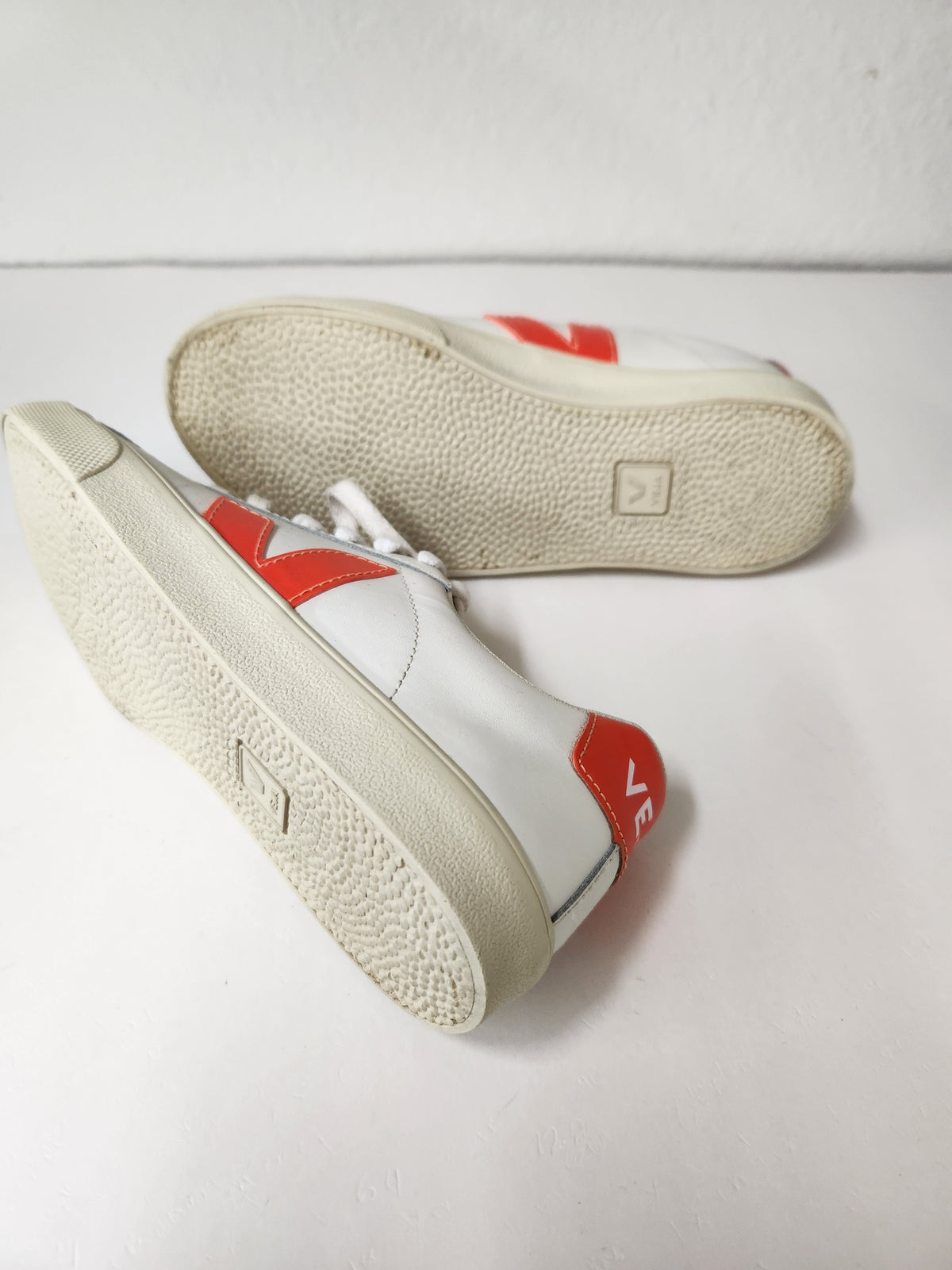A pair of white leather low-top sneakers with red accents, shown from the side and sole on a light gray surface.