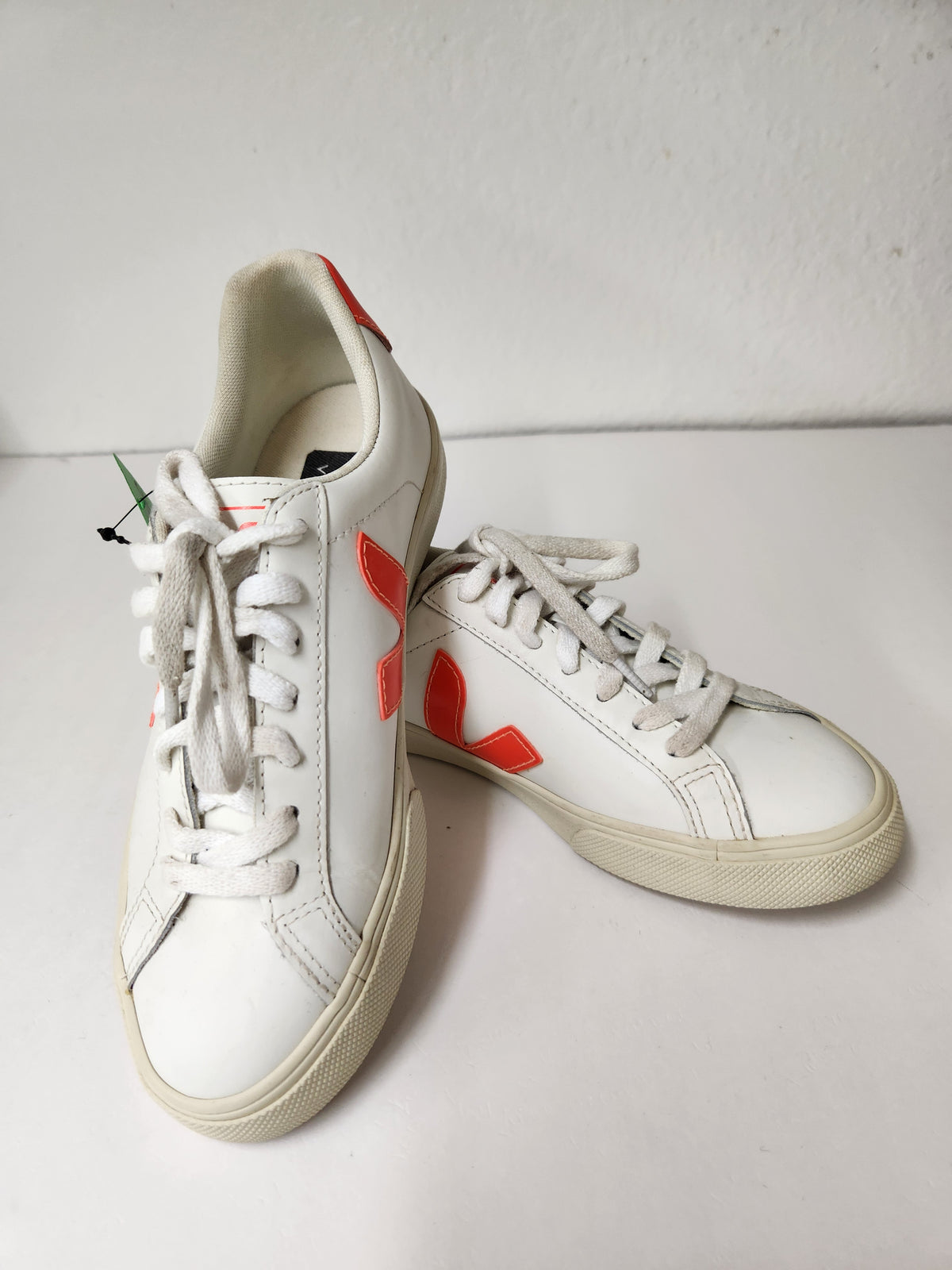 A pair of white leather low-top sneakers with vibrant red side logos and white laces, displayed on a white surface against a white wall.