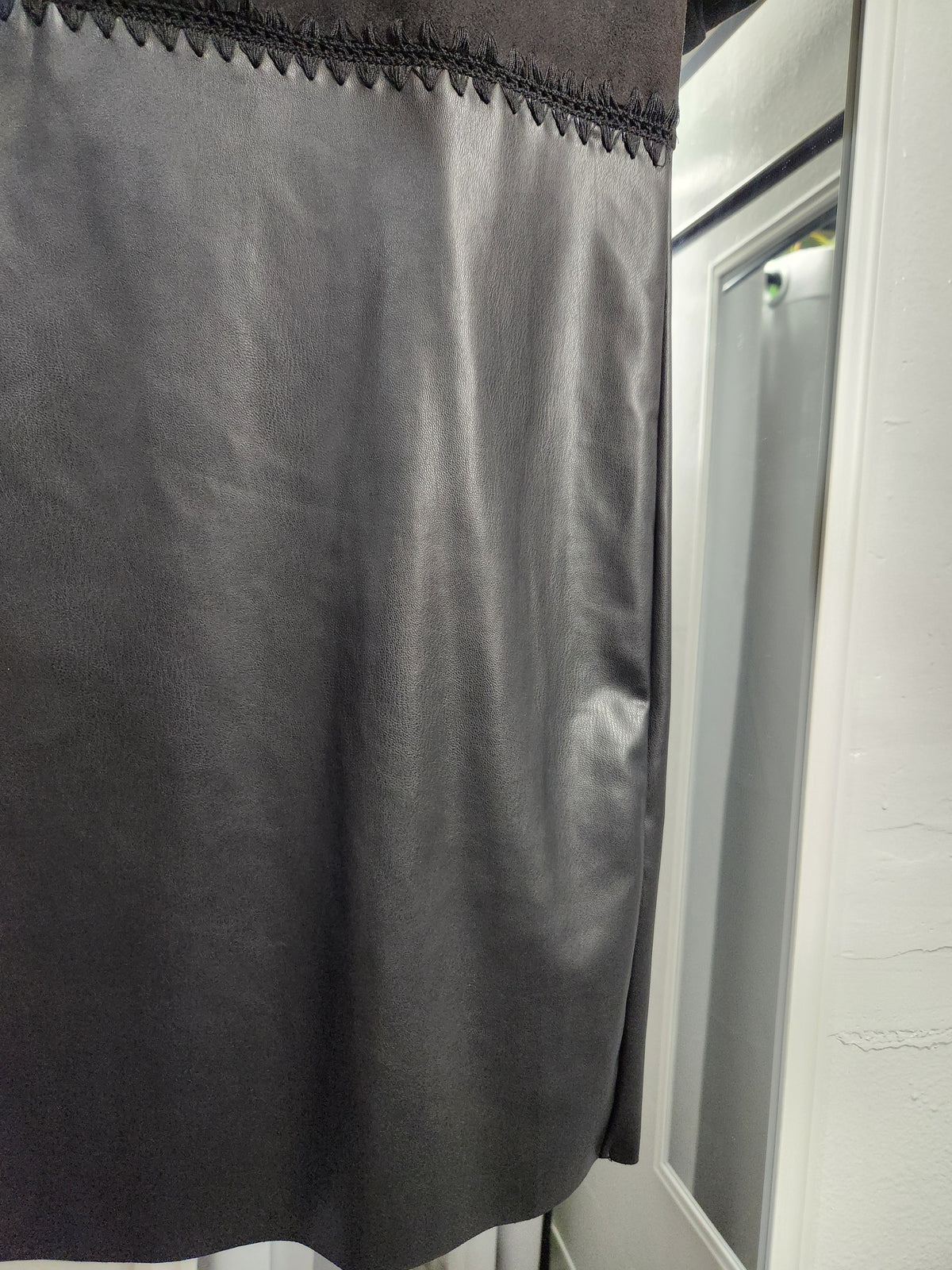 A close-up of a dark gray curtain panel with a decorative embroidered border at the top, shown hanging next to a white window frame.