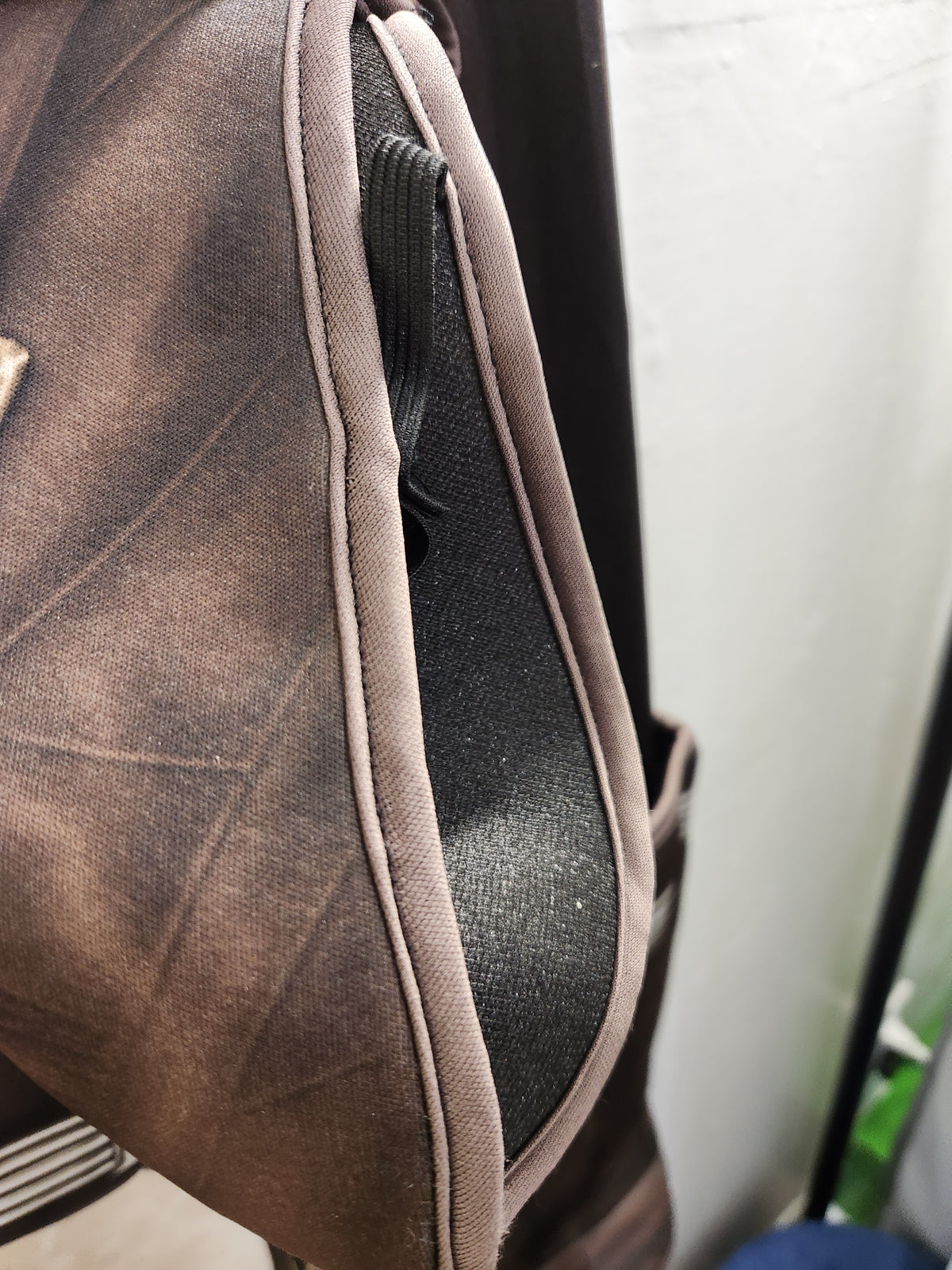 Close-up of a brown canvas or leather-like bag with a dark zipper track and a light beige piping border, photographed indoors against a light wall.