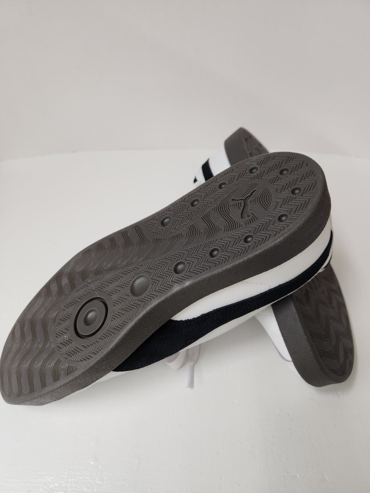 A pair of low-top sneakers shown from the sole side, featuring a dark gray textured rubber outsole, a white midsole, and a black and white upper.