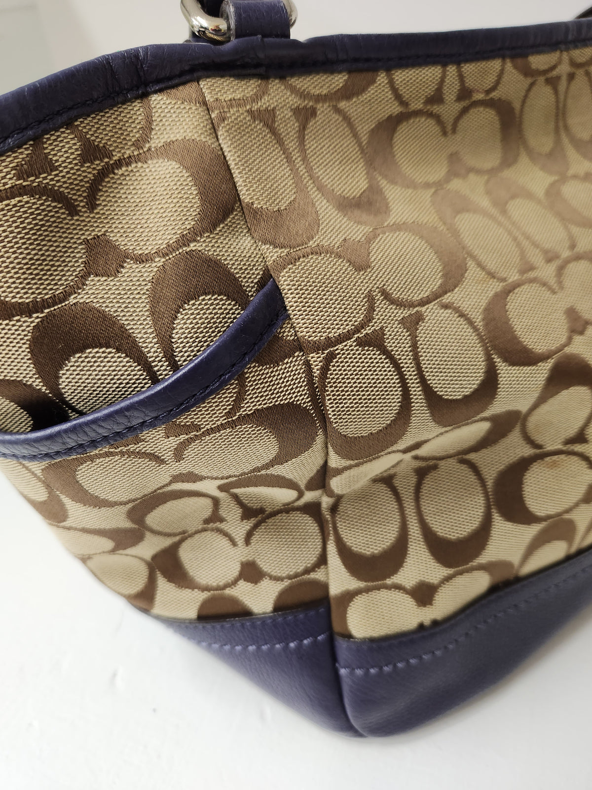 Close-up of a Coach handbag featuring the signature monogram canvas in beige and brown with dark navy blue leather trim.