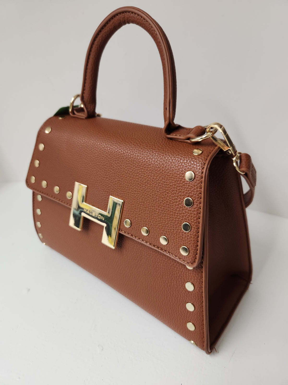 A brown textured leather handbag with a top handle, studded edges, and a prominent gold-tone H-shaped metal clasp on the front flap.