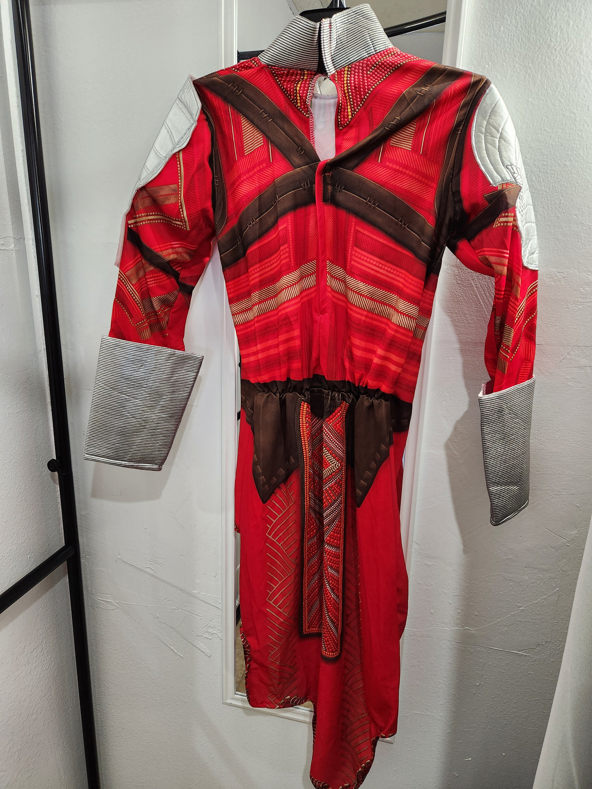 A red and brown patterned long-sleeve dress with gray quilted shoulder panels and cuffs, hanging on a black hanger against a white wall. Wakanda's Dora Milaje Adult Costume