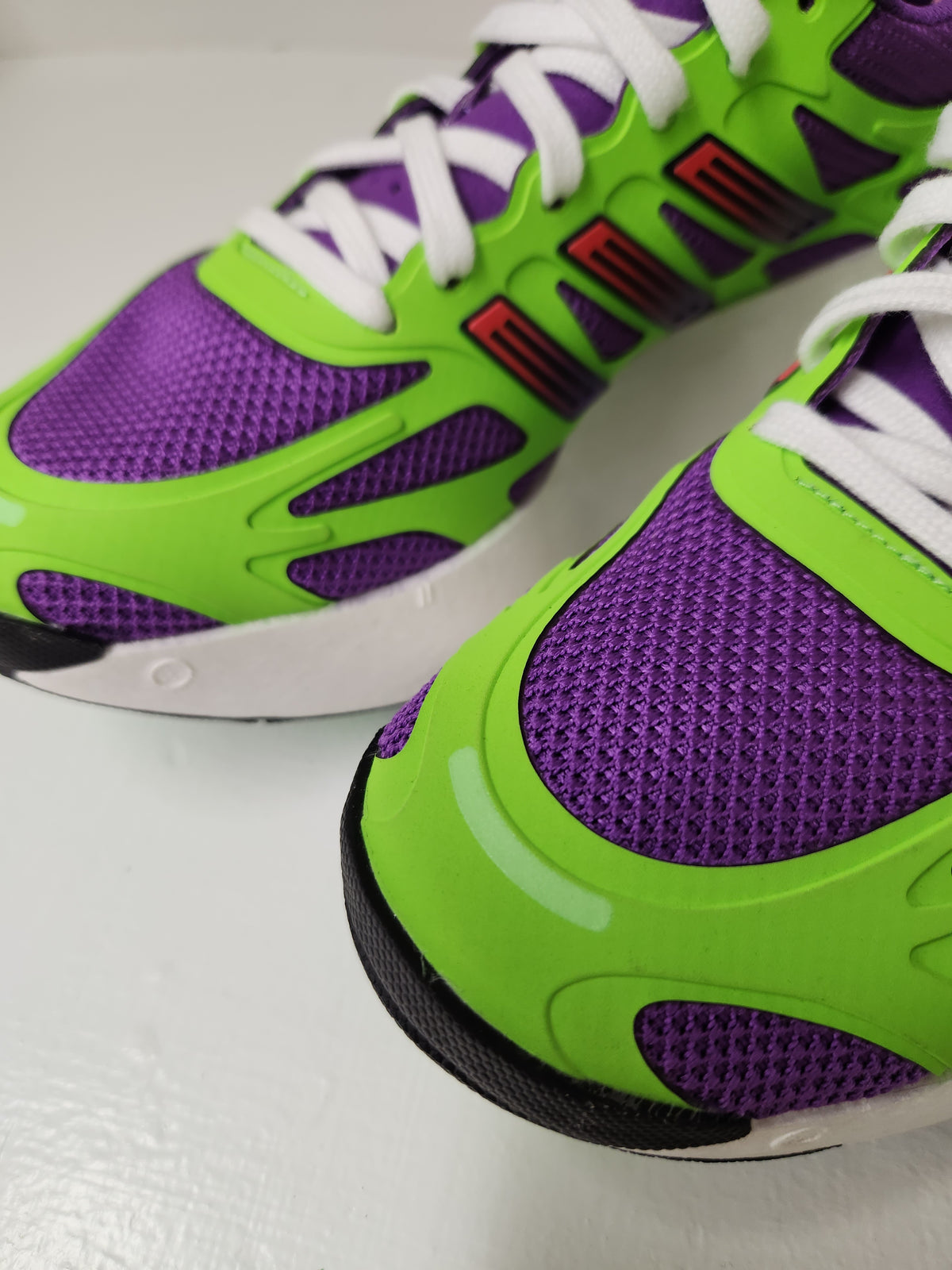 A close-up of a pair of athletic sneakers featuring a vibrant lime green and purple color scheme, with white laces and red accents on the side.