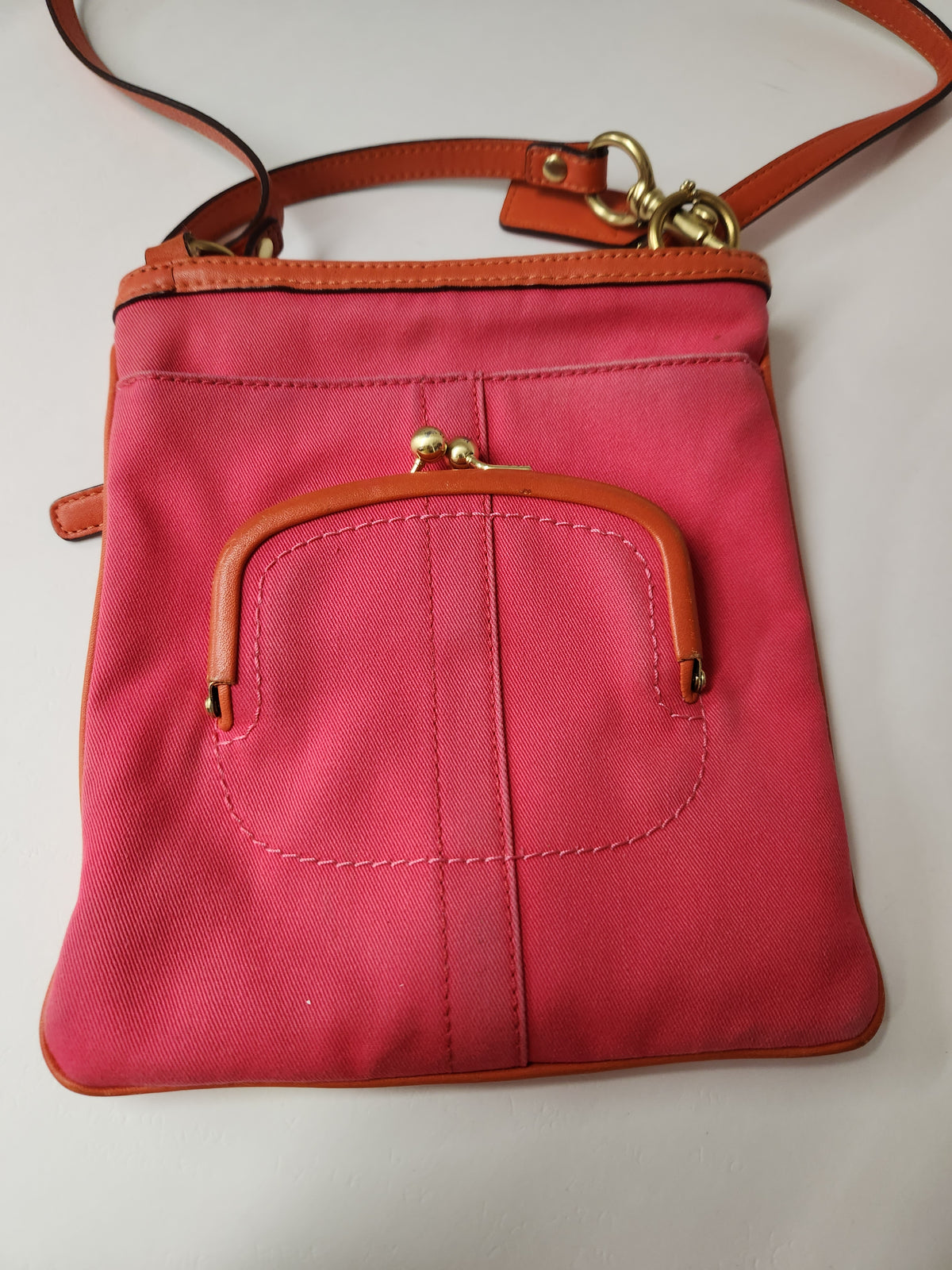 A pink canvas shoulder bag with brown leather trim and a gold-tone kiss-lock clasp on the front pocket, shown against a plain light background.