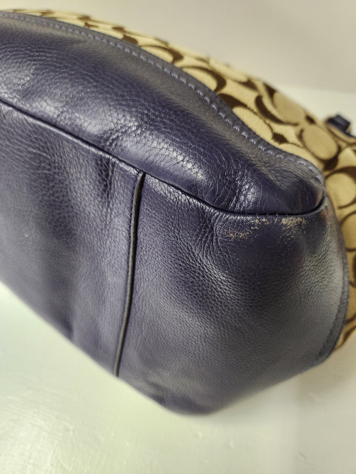 Close-up of a Coach handbag showing a dark navy pebbled leather base and the signature beige and black Coach logo pattern on the side.