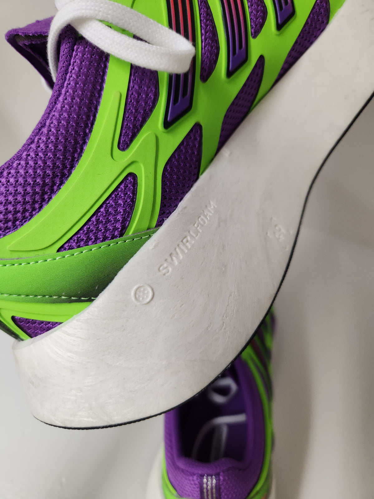 Close-up of a purple and neon green athletic sneaker with a thick white sole, showing the side profile and textured mesh upper.