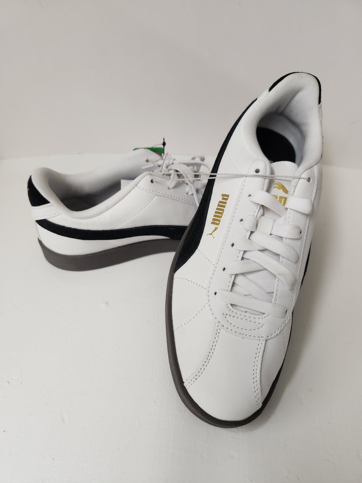 A pair of white Puma sneakers with black side stripes and a gold Puma logo, displayed on a light gray background.