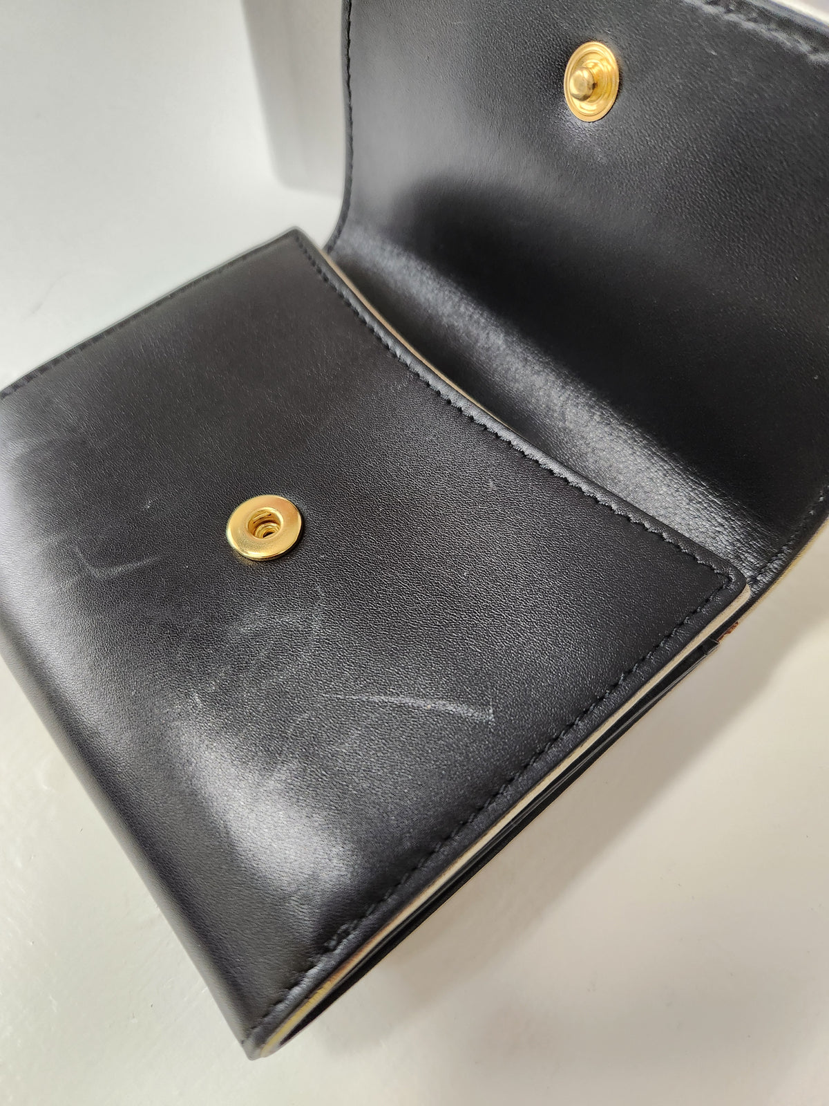 A versace black leather wallet shown open, featuring two gold-tone snap buttons and visible wear scratches on the exterior surface.