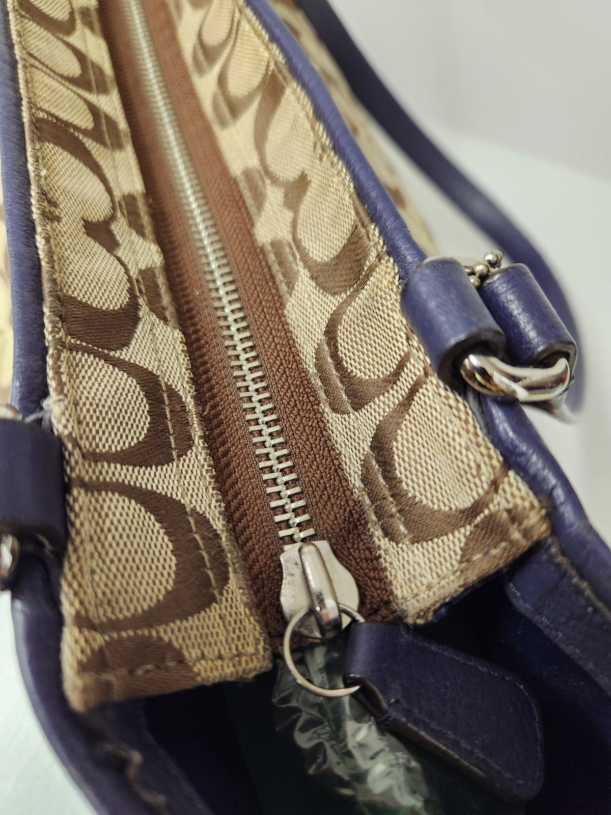 Close-up of a Coach handbag showing the signature monogram canvas zipper track, silver zipper, and dark blue leather trim.