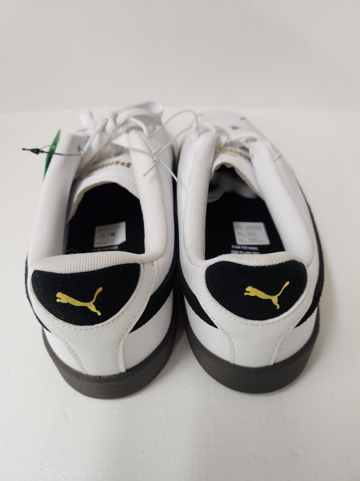 A pair of white Puma sneakers viewed from the back, featuring black heel tabs with yellow Puma logos and white laces, set against a plain light background.