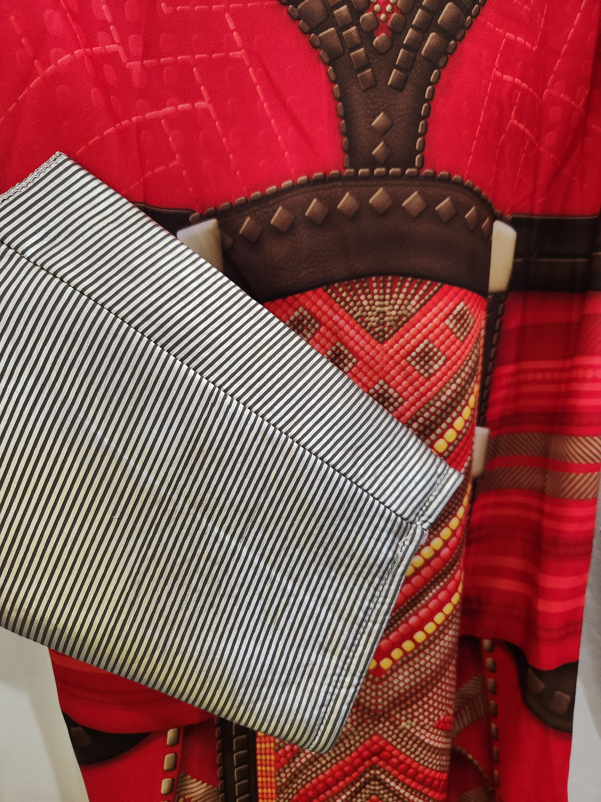 A close-up of a silver and black striped fabric clutch bag layered over a red and brown patterned garment.