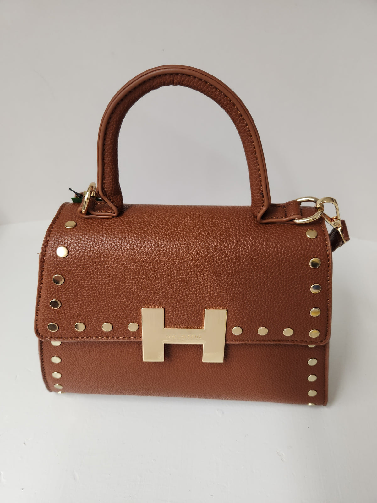 A brown pebbled leather handbag with a top handle, gold-tone studs, and a large gold H-shaped metal clasp on the front, photographed against a plain light background.