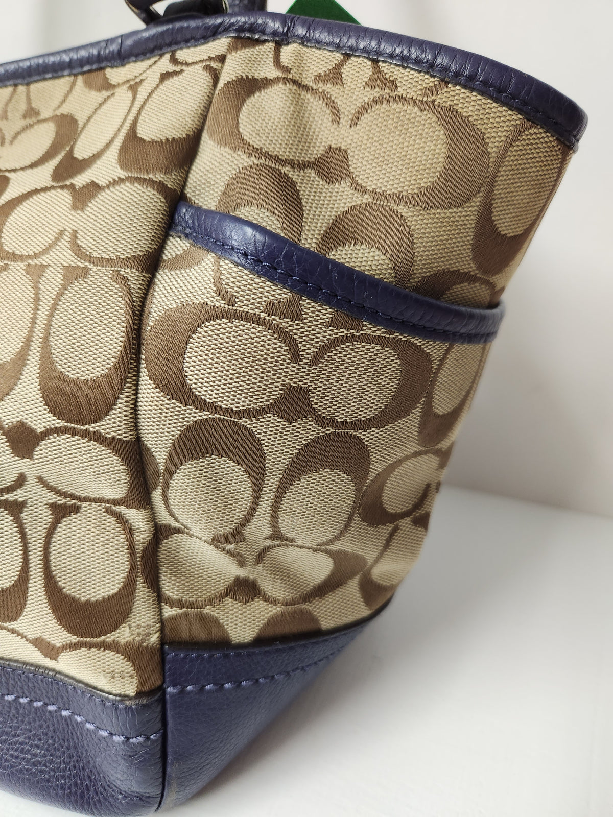 Close-up of a Coach handbag featuring the signature beige and brown monogram canvas with navy blue leather trim and base.
