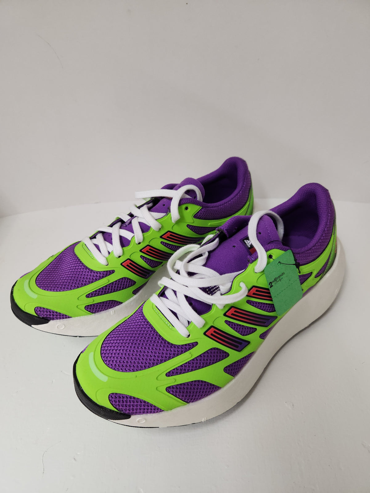 A pair of athletic sneakers in bright lime green and purple with white laces and black accents, photographed on a plain light background.