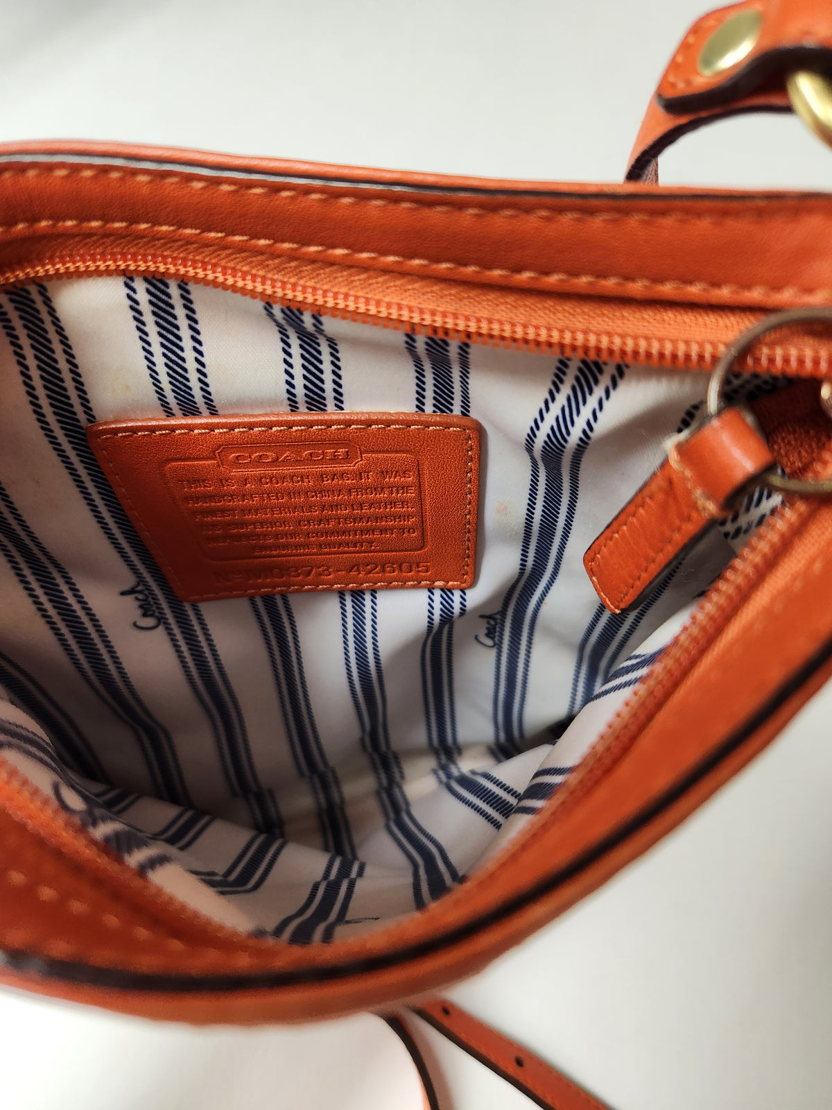 Close-up of an orange-brown leather Coach handbag interior, showing a striped white and navy lining and a branded leather patch inside the compartment.