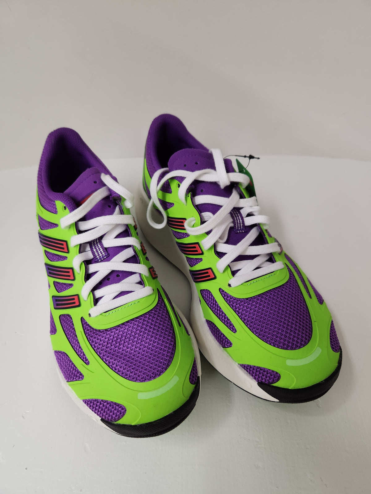 A pair of athletic sneakers in purple and neon green with white laces, photographed on a plain light background.