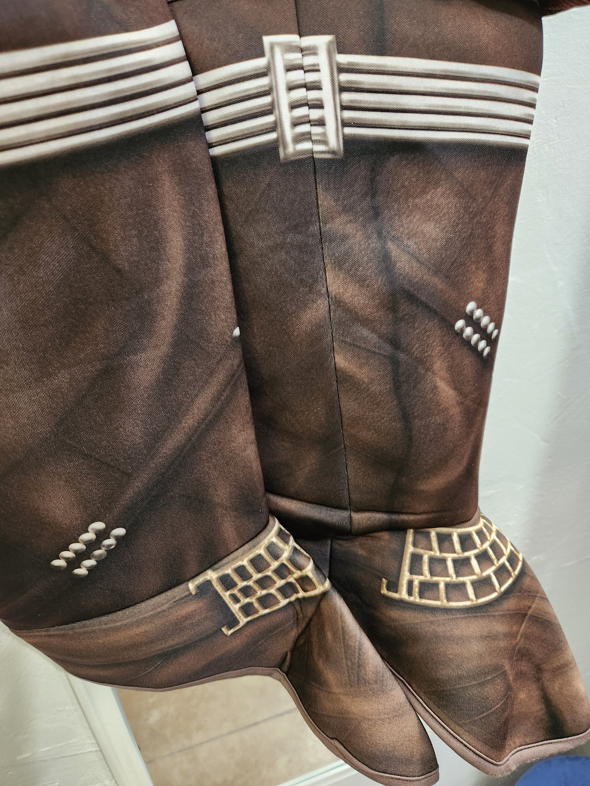 A pair of brown faux-leather cowboy boots with western-style metallic gold and silver decorative straps, studs, and buckles, shown against a neutral indoor background.